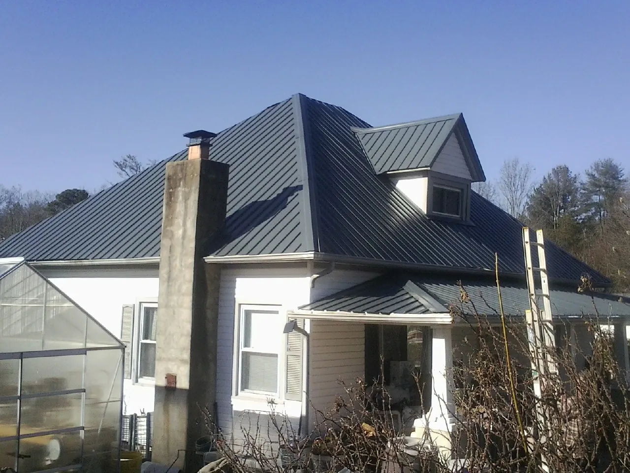 Dark blue standing seam metal roof on a white farmhouse with dormer — Slate & Tile Roof Repair by Roofing Brothers in Wilder