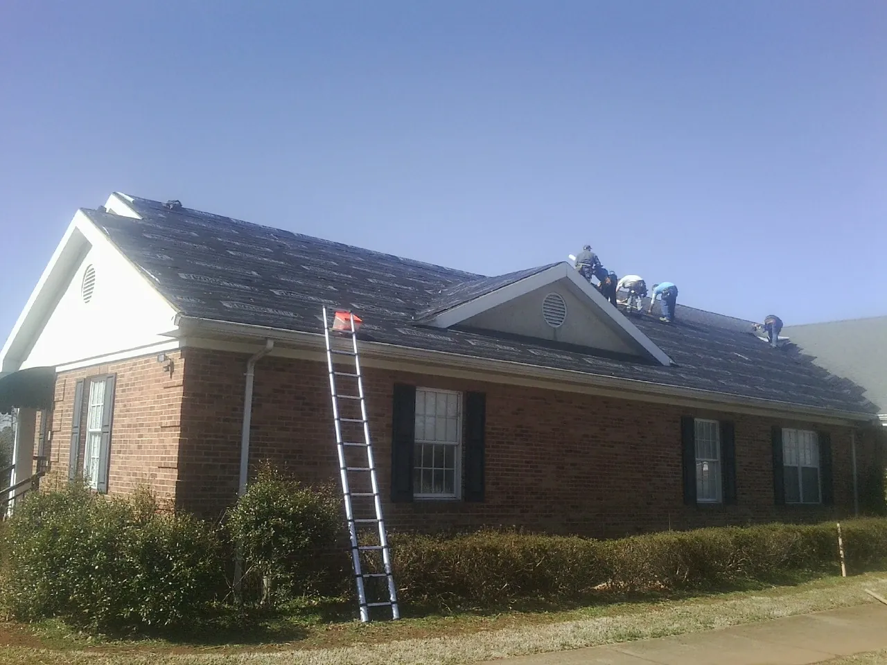Crew tearing shingles off a brick ranch roof with a ladder set — Metal Roof Repair work by our crew in Wilder