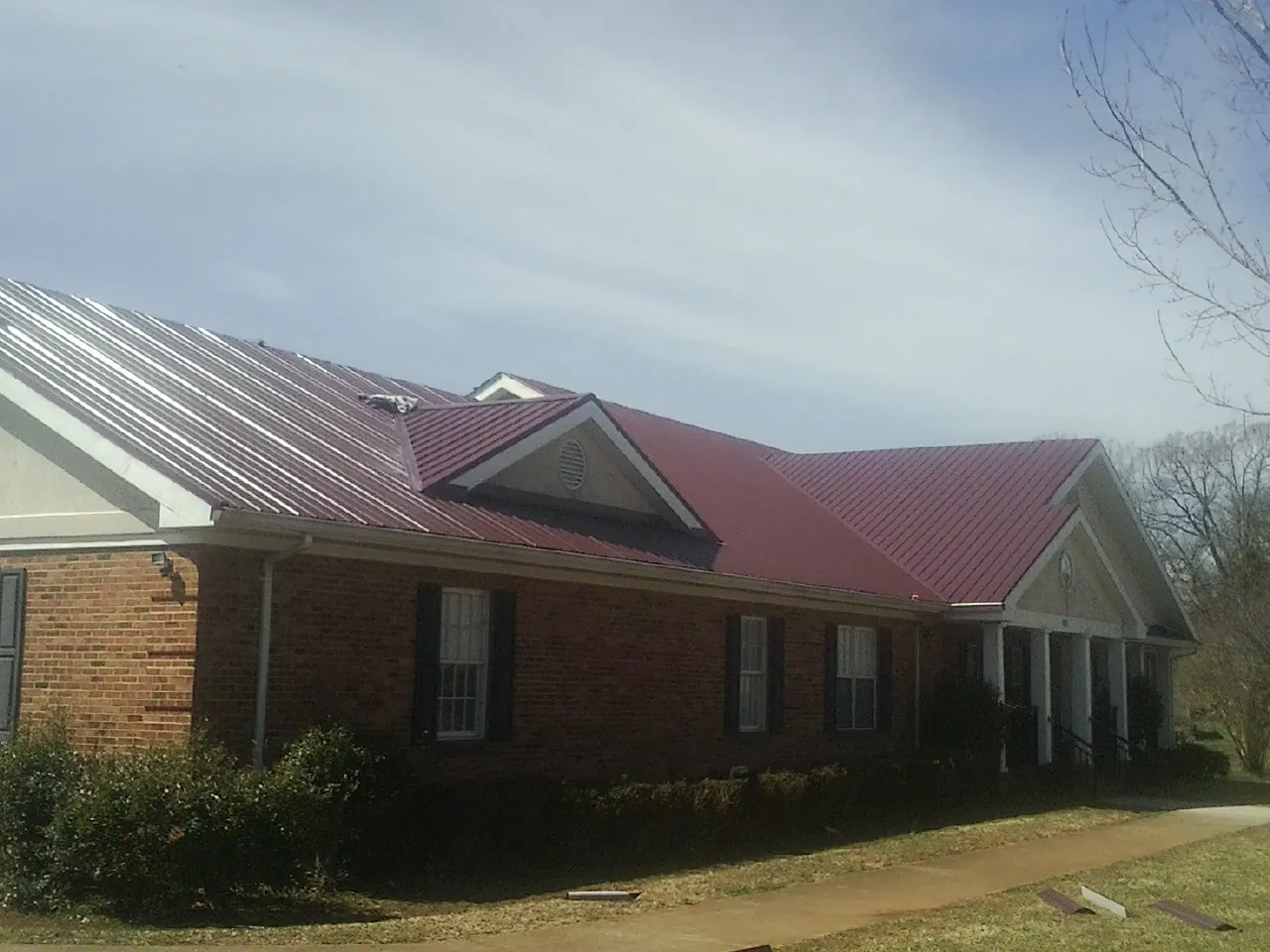 Red metal roof with gabled entries on a long brick building, from a Hail Damage Roof Repair job in Wilder