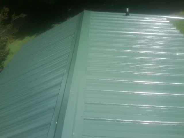 New green metal panels meeting at the ridge of a roof — Flat Roof Repair work by our crew in Wilder